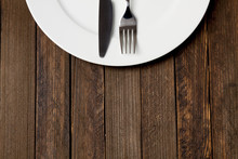 Fork And Knife With White Plate On Dark Wooden Background, Empty Space On Bottom