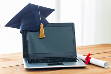 Wall Mural - close up of laptop with mortarboard and diploma