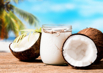 coconut oil and fresh coconuts on black stone with tropical beach background