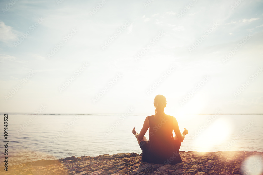 Young woman doing meditation practice on the beach. Intentional sun glare and lens flare effect - obrazy, fototapety, plakaty 