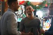 © Connect Images - Young man in public house holding beer bottle looking at friend smiling