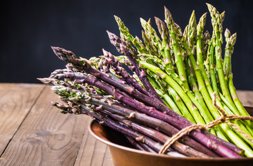 Asparagus bunches green and purple on dark wooden background.