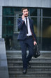 © amixstudio - A businessman walks down the stairs and talking on mobile phone holding a briefcase against the building with a glass facade