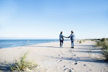 Two Young Women, Walking Along Beach, Holding Hands, Rear View
