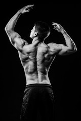 Wall Mural - Young and fit bodybuilder athlete demonstrates biceps back view isolated on black background