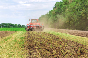 Wall Mural - Modern tech red tractor plowing a green agricultural field in spring on the farm. Harvester sowing wheat.