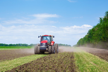 Wall Mural - Modern tech red tractor plowing a green agricultural field in spring on the farm. Harvester sowing wheat.