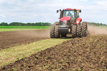 Wall Mural - Modern tech red tractor plowing a green agricultural field in spring on the farm. Harvester sowing wheat.