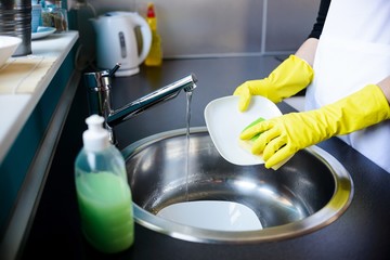 Wall Mural - Woman washing dishes in the kitchen with sponge.