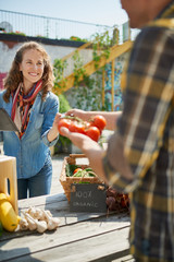 Wall Mural - Friendly woman tending an organic vegetable stall at a farmer's market and selling fresh vegetables from the rooftop garden