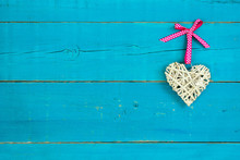 Wicker Heart With Pink Ribbon Hanging On Teal Blue Background
