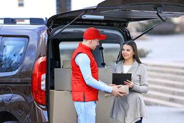 Wall Mural - Delivery man and attractive young woman receiving a package, near the car outdoors