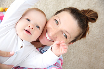 Wall Mural - Young mother taking a selfie with her baby on the floor, close up