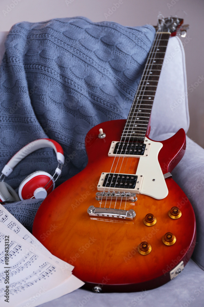 Electric guitar with notes and headphones on grey sofa