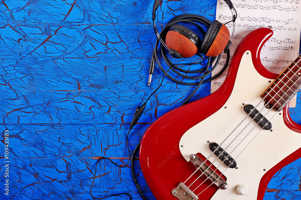 Electric guitar with headphones and notes on blue wooden background