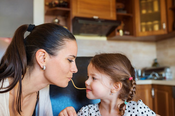 Mother and daughter in the kitchen, eating spaghetti together