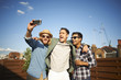 © Connect Images - Three male friends taking camera selfie at rooftop party