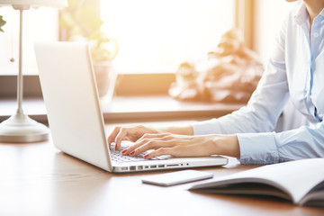 Cropped portrait of female entrepreneur developing business plan using laptop indoor. Side close up view of young woman writer working on new book, typing on computer against home interior background