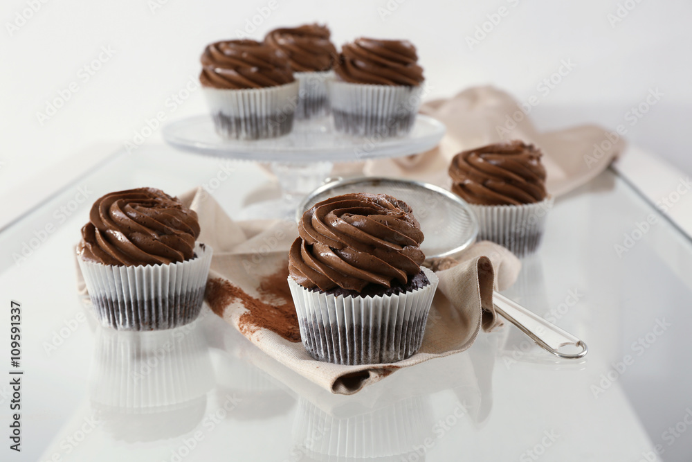 Chocolate cupcakes with sieve on light glass background