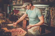 Handsome Pizzaiolo Making Pizza At Kitchen In Pizzeria.