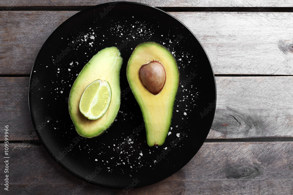 Sliced avocado with lime and salt on black plate