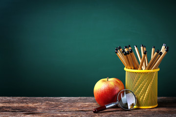 Wall Mural - Set of pencils in metal holder, magnifier and apple on blackboard background