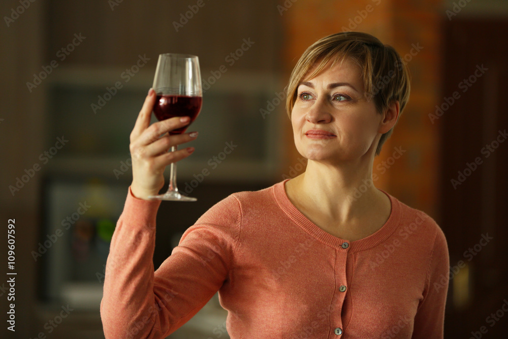 Beautiful middle-aged woman tasting red wine, indoors