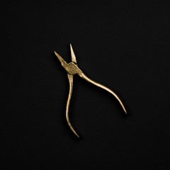 Golden pliers isolated on black background. Symbolic repair tool