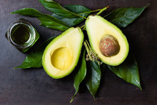 Avocado With Leaves And Jar Of Oil On Black Background