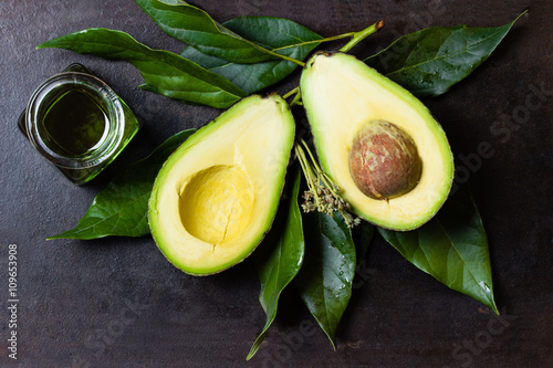 Fotografie, Obraz Avocado with leaves and jar of oil on black background