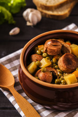 Wall Mural - Vegetable stew with pork sausages on dark beer in ceramic bowl on a dark wooden background with garlic, herbs and bread 