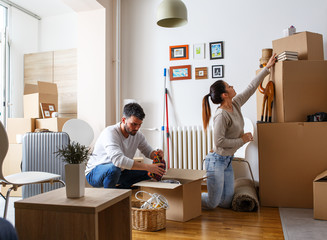 Wall Mural - Young married couple moving into new home. They're unpacking card boxes with their accessories.