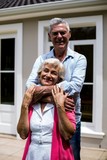 Fototapeta Zwierzęta - Smiling senior couple standing with arms around at yard 