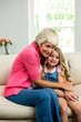 © WavebreakmediaMicro - Smiling granny and girl hugging while sitting on sofa