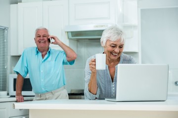 Happy woman using laptop while senior man talking on phone 