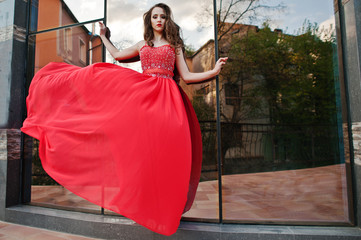 Portrait of fashionable girl at red evening dress posed backgrou