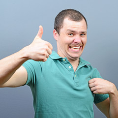 Wall Mural - Portrait of a man showing thumb up or ok sign against gray backg