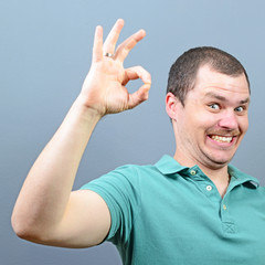 Wall Mural - Portrait of a man showing thumb up or ok sign against gray backg