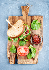 Chicken, sun-dried tomato and spinach sandwich with spicy sauce on rustic wooden board over grey concrete textured background