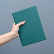 Hand holding green book against gray background