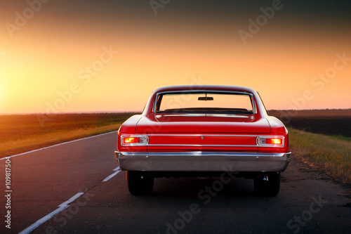 Retro red car standing on asphalt road at sunset Poster