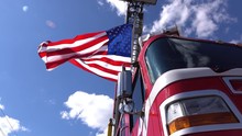 Parked Red Emergency Response Vehicle Holds Waving American Flag From Ladder Under Blue Sky.
