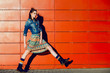Young teenager girl posing, going, runs near urban red wall background in skirt and jeans jacket on the sunset.