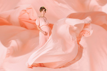 Pregnant woman dancing in pink evening dress flying on wind. Waving fabric, fashion shot.