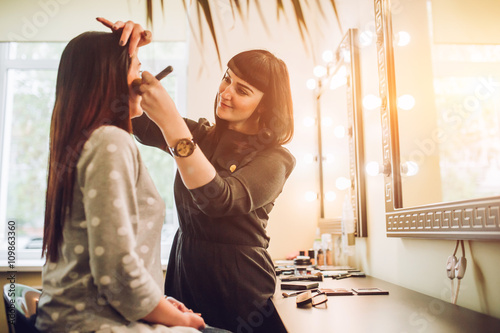 Fotografía Professional expert,makeup artist prepares very beautiful,young,well-known,glamorous,stunning model for filming shooting for cover of fashion magazine VOGUE,does make-up,makes up lips,art,eyes,white
