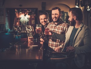 Wall Mural - Cheerful old friends having fun and drinking draft beer at bar counter in pub.