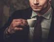 © Nejron Photo - Serious well-dressed hispanic man with cup of coffee posing on dark background.