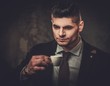 © Nejron Photo - Serious well-dressed hispanic man with cup of coffee posing on dark background.