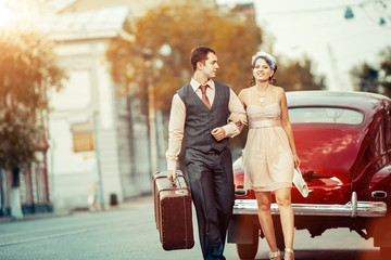 Pretty walking couple with the suitcase on the vintage car backg