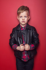 Wall Mural - Fashion little boy wearing a leather jacket. Studio portrait over red background